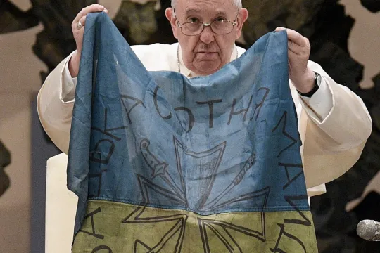 A handout picture provided by the Vatican Media shows Pope Francis holding a flag of Ukraine that was sent to him from the Ukrainian town of Bucha during the weekly general audience in the Paul VI Audience Hall, in Vatican City, 06 April 2022. The pontiff lamented the 'massacre of Bucha', in the Kyiv suburb where dozens of bodies in civilian clothing have been found, and renewed his calls for an end to the war in Ukraine. EPA/VATICAN MEDIA HANDOUT